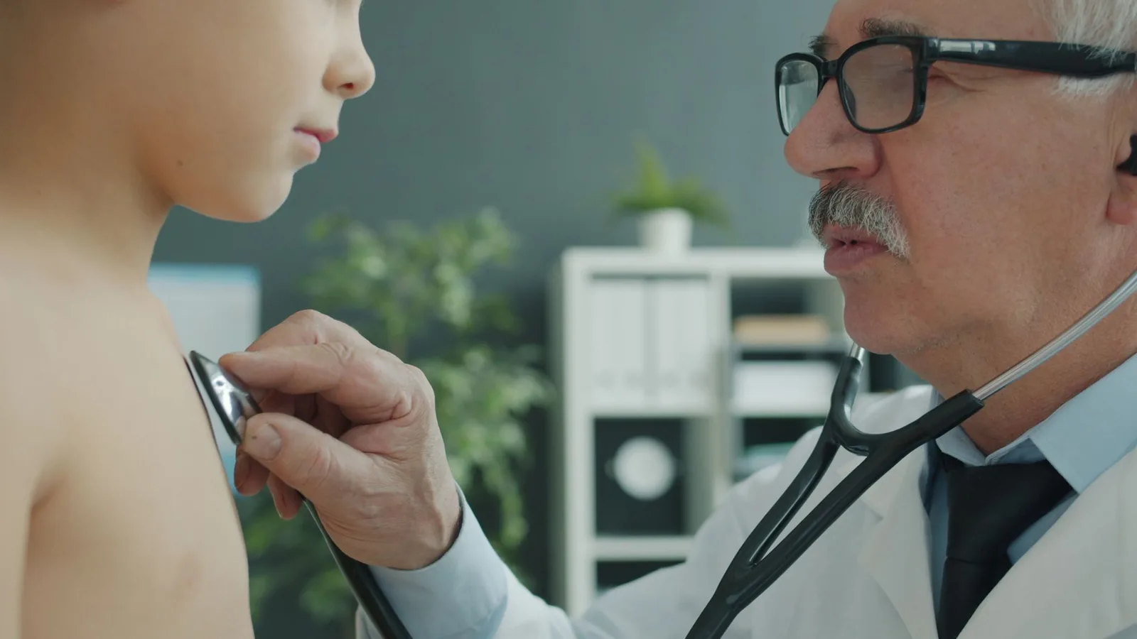 Senior doctor examines young patient with stethoscope in modern clinic.