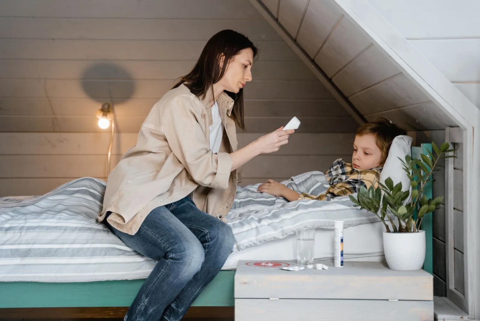 Mother checking son's fever with a digital thermometer, showcasing health care and parenting.