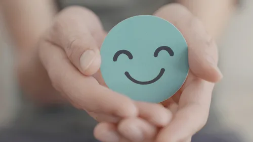 Child's hands holding turquoise circle with smiling face drawn on it.