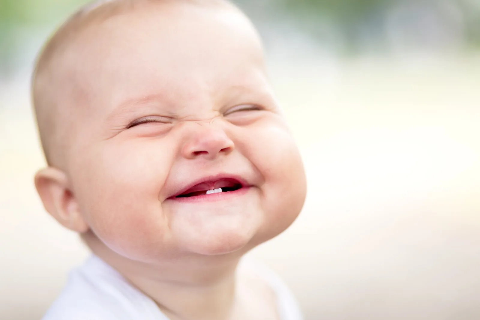Happy infant with closed eyes and open mouth smiling outdoors.
