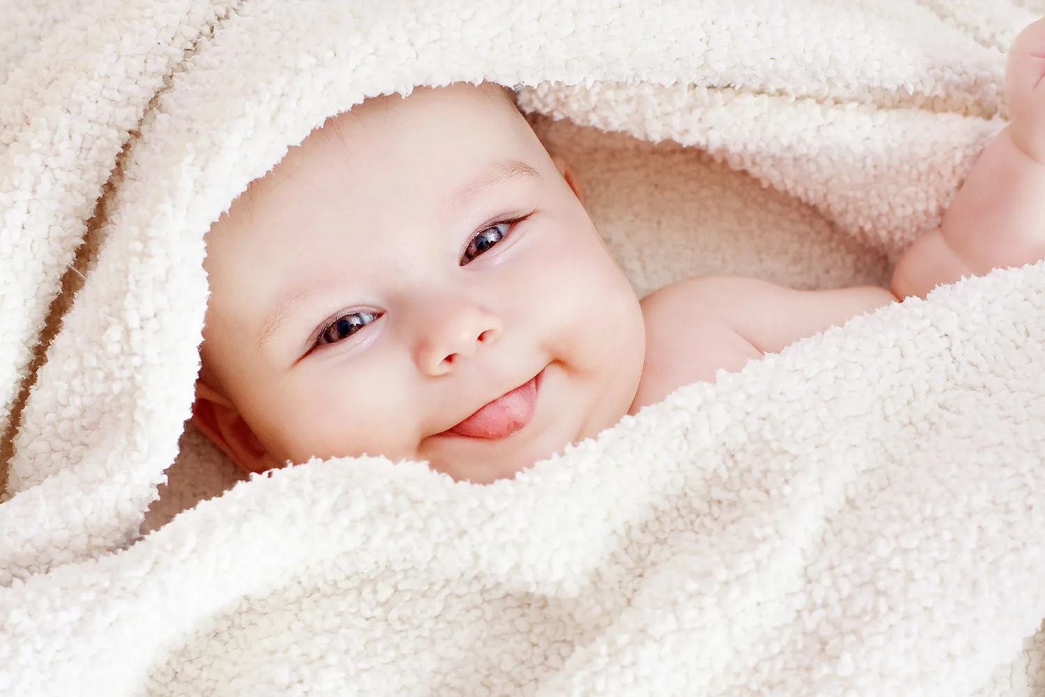 Smiling newborn baby wrapped in soft white blankets, looking at camera.