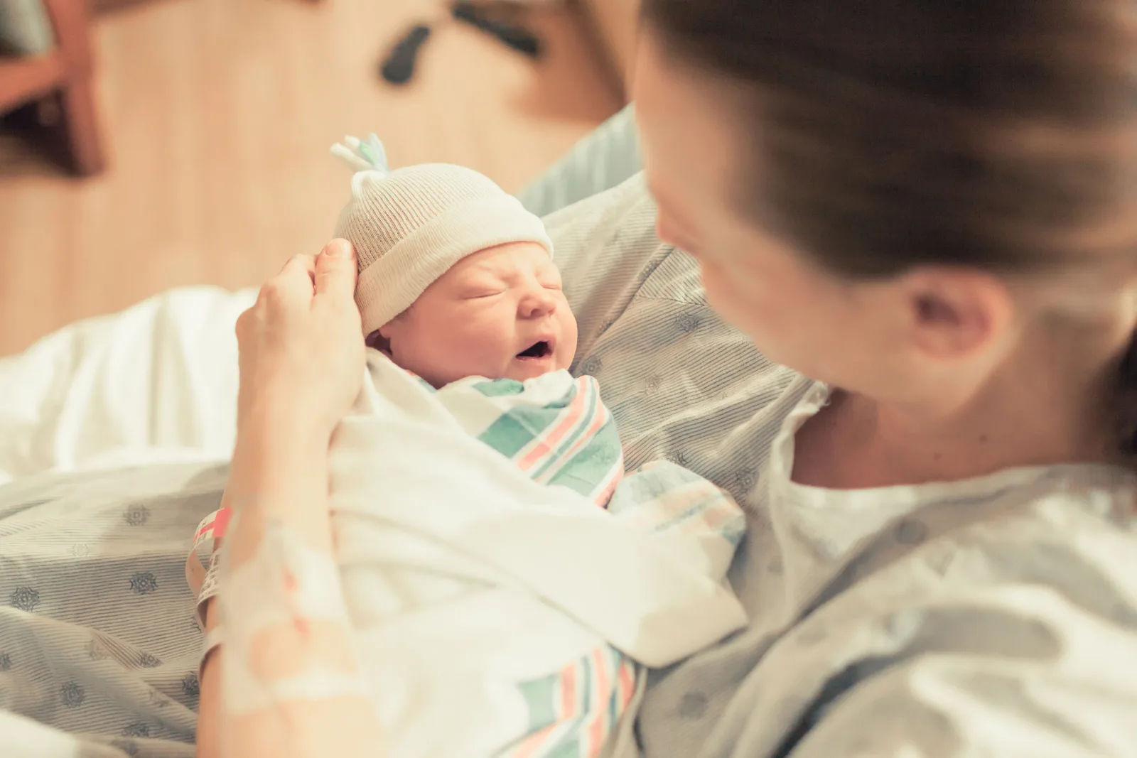 Newborn baby wearing white hat and striped outfit held by adult caregiver.