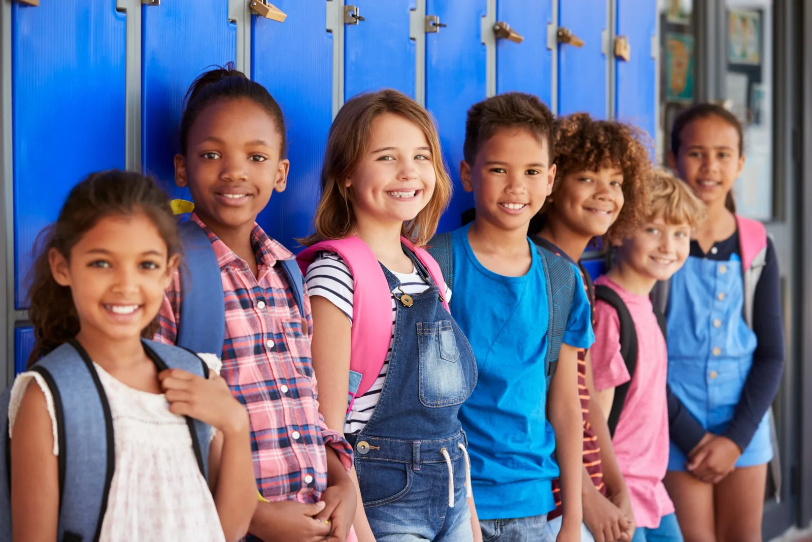 Diverse group of smiling children standing in front of blue school lockers.