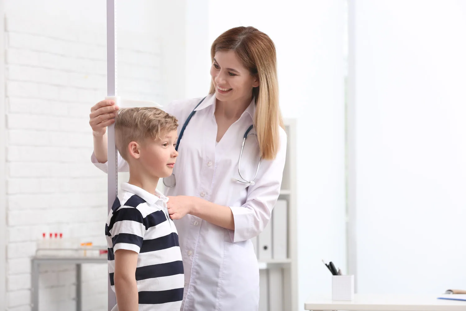 Female pediatrician measuring young boy's height against wall-mounted scale.
