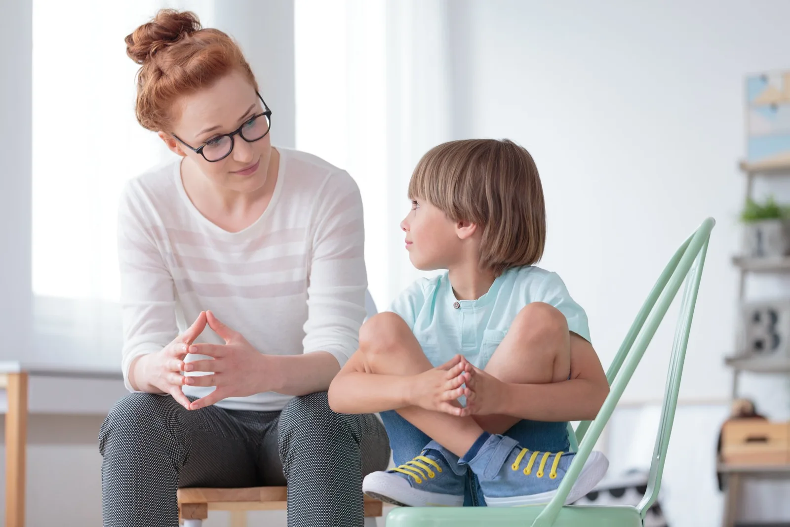 Pediatrician with glasses speaking with young child in bright clinical office setting.